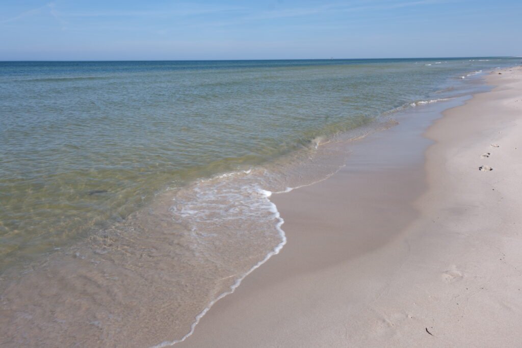 Szeroka, piaszczysta plaża z delikatnie falującym, czystym Bałtykiem przy brzegu.