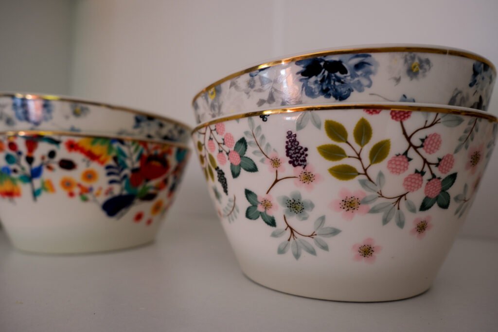Zbliżenie na porcelanowe filiżanki ozdobione kolorowymi kwiatami i złotym rantem – detale domowej atmosfery.