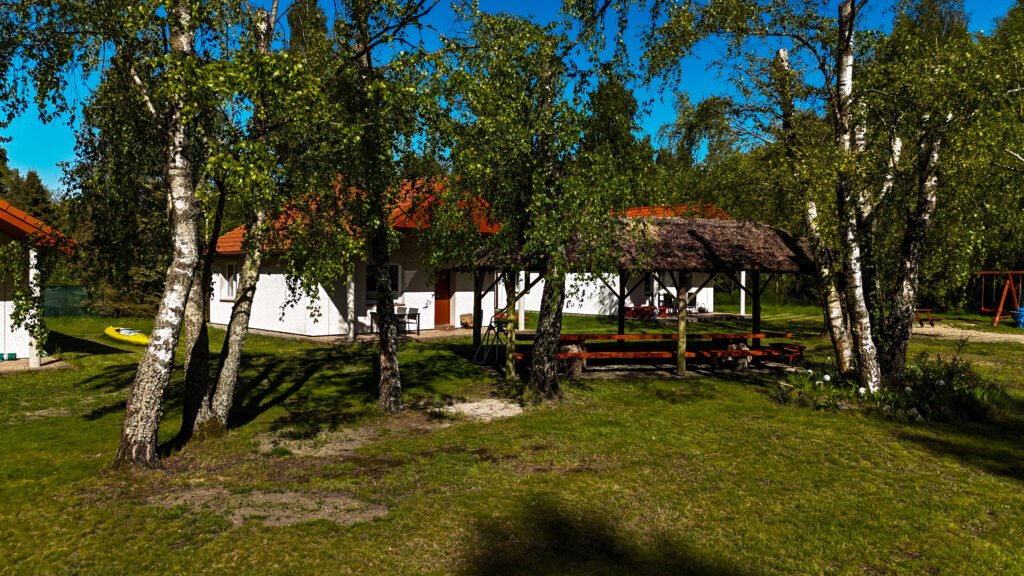 Widok na domki i altanę wśród drzew – spokojna, zielona przestrzeń.
