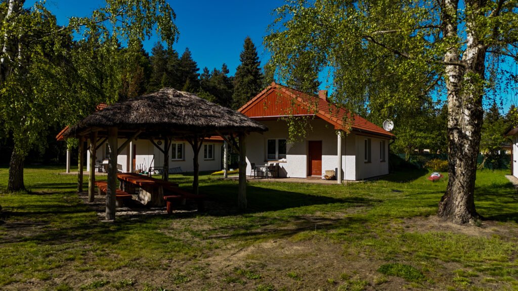 Widok na domki i altanę wśród drzew – spokojna, zielona przestrzeń.