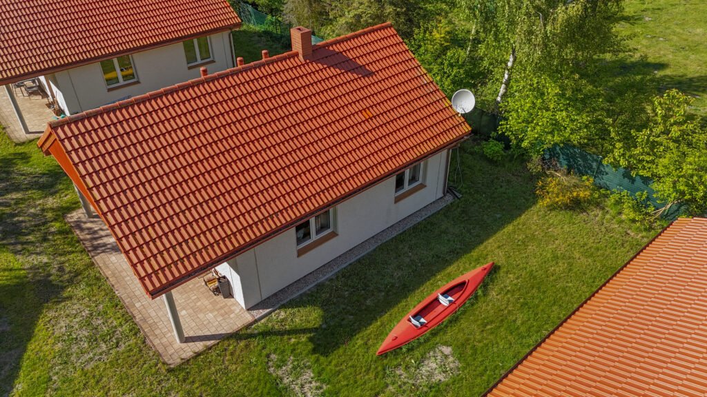 Domek z czerwonym dachem widziany z lotu ptaka, z kajakiem leżącym na trawie obok.